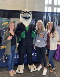 Three women smile a pose with a college mascot