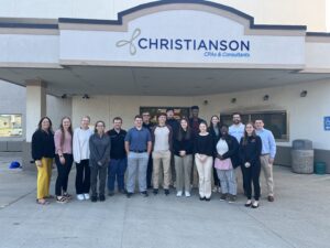 A diverse group of individuals gathered in front of the Christianson Building, showcasing community and collaboration.