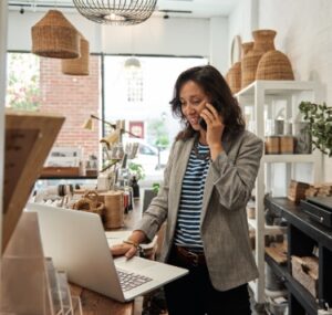 woman in a shop looking at laptop and talking on the phone