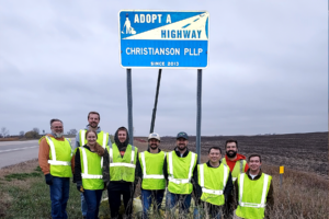Nine Christianson employees in neon pose in front of an 'adopt a highway' sign