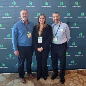 Three individuals pose in front of a green energy banner, promoting sustainable practices and renewable energy solutions.