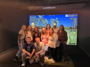 Friends gathered together, posing happily for a photo in front of an exciting video game display.