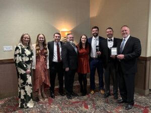 A team of people stands in a room, joyfully displaying an award, symbolizing their collective success and teamwork.