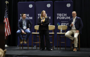 Three attendees at a tech forum, seated on chairs, exchanging ideas and insights in a collaborative environment.