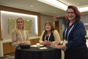 Three women at a business conference stand next to each other and smile