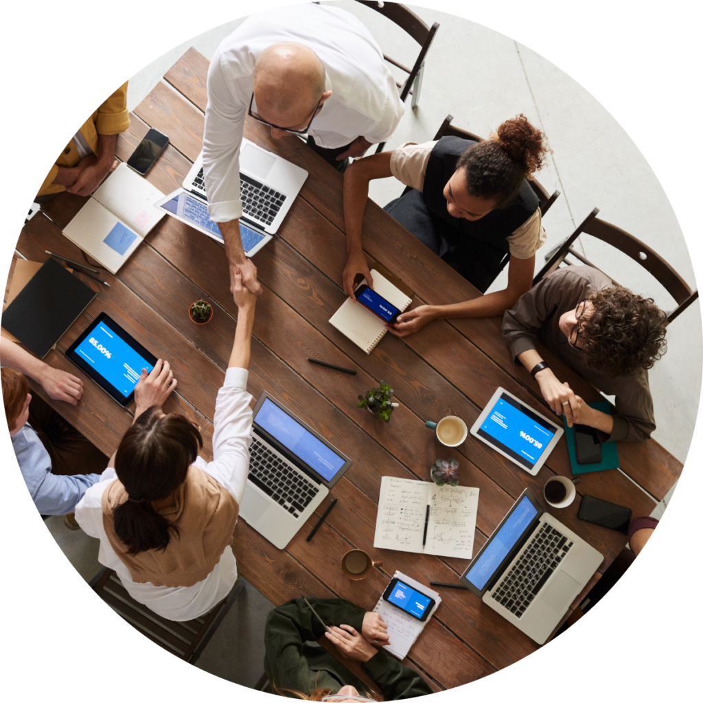 Group of people collaborating at a table, using laptops and tablets for discussion and teamwork.
