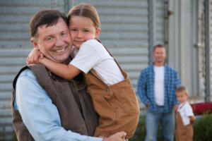 A grandfather embraces a little girl in front of a weathered barn, highlighting a sweet and affectionate family interaction.