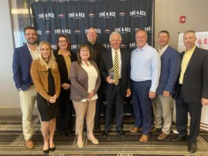 John Christianson stands holding ACE award surrounded by diverse group of employees