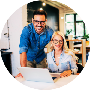 Smiling man and woman look directly at the camera from behind a laptop