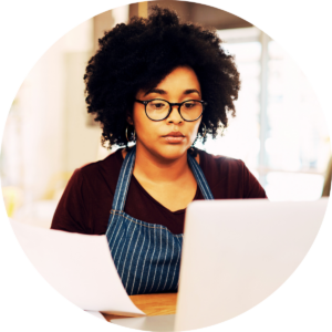 Woman in apron looking at a computer laptop and paperwork