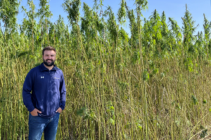 A smiling employee stands in front of a hemp field