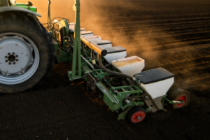 A tractor uses a seeder to plant seeds in a freshly tilled field