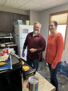 A man and a woman smile at the camera while making pancakes.